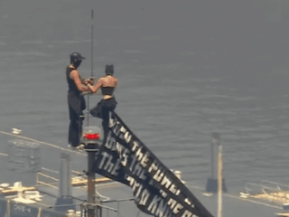 Two individuals climb on high of the Empire State Constructing with message on banner
